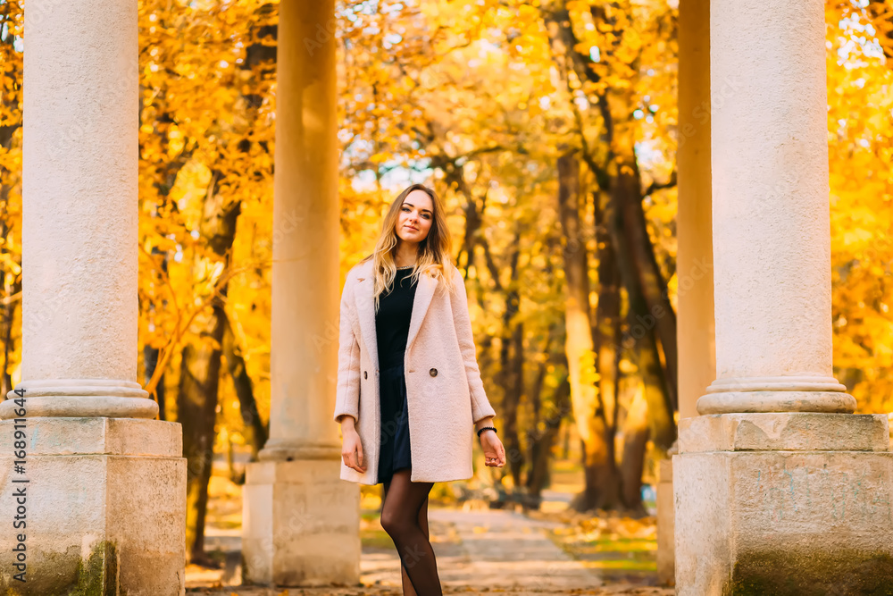Beautiful woman posing for camera near columns in autumn orange