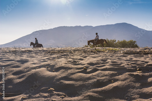 riders on horses on the beach during sunny day, mountains on the horizon, Italy, Sardinia island, activity on the beach
