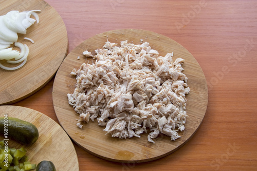 Finely chopped pickled cucumber on the board and a cutting knife; Boiled chicken, onions on the wooden table top