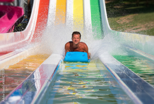 Valokuva Attraktiver Mann hat Spaß auf einer bunten Wasserrutsche in einem Aquapark