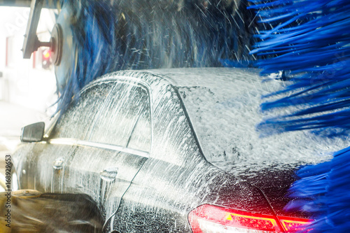 Car wash, black car in automatic car wash, rotating red and blue brush. Washing vehicle.