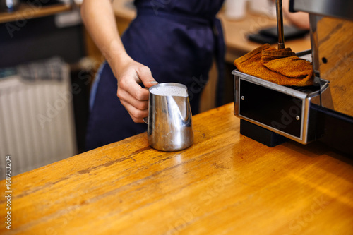 Barista prepares coffee cappuccino, pouring foamed milk into a cup