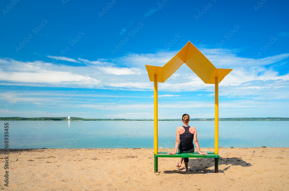 Silhouette of a girl sitting on a yellow metal bench with a canopy from the sun on the beach. Relaxation and recreation concept. Long exposure