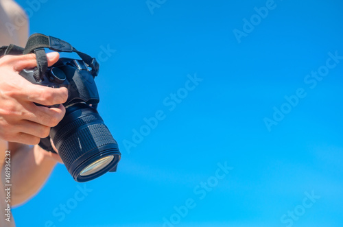 Dslr camera in the hands against the blue sky. The photographer viewing the captured image and adjusts the camera. Сlean space for background