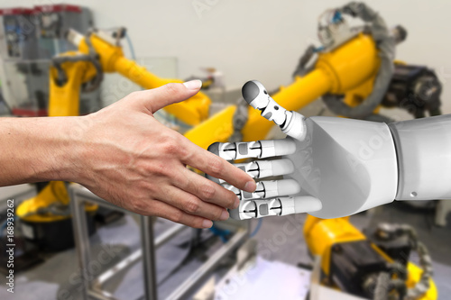Artificial intelligence (AI) advisor or robo-adviser technology. Shaking hands of male and automation robot with blur automation arm in smart factory background.