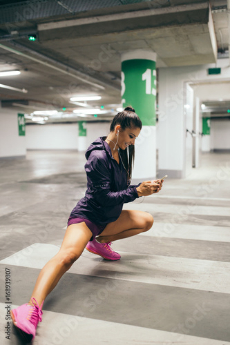 Beautiful athletic woman reading messages on mobile phone in public garage.  © hedgehog94