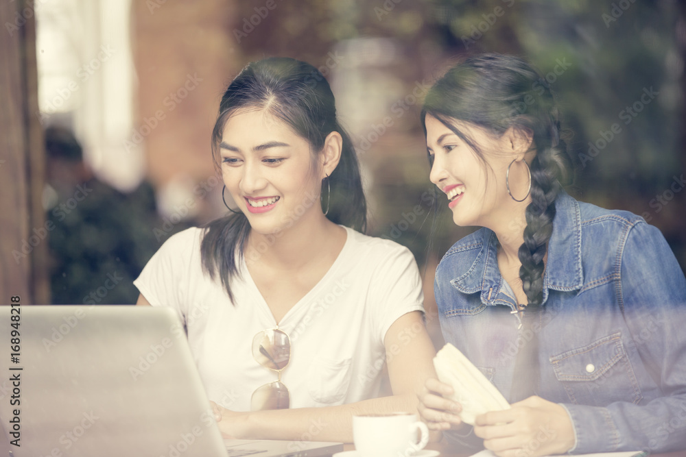Asian Woman using Laptop at Cafe with Attractive Smiling Together, Woman Talking with Friend while using Laptop, Woman Lifestyle Concept, Vintage Tone.