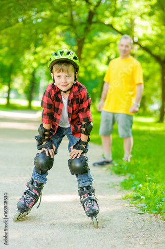 Portrait of a boy in a protective helmet and protective pads for roller skating on the background of his father