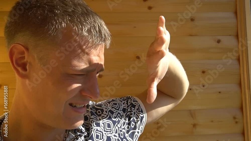 portrait of young man looking away and covering their face with a hand against the sun's rays.