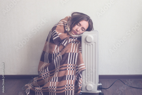 young woman in woolen plaid warm up hands over electric heater