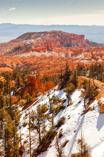 Deep red rocks form hoodoos and plateaus across the snow covered trees and ground