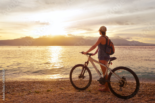 Traveler with bike enjoying the sunset on the background of the island