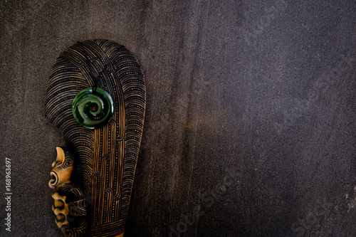 New Zealand - Maori themed objects - mere and greenstone pendant on gray stone background