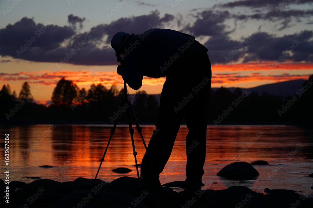 Silhouette of photographer framing a shot, taking pictures on the river at sunset