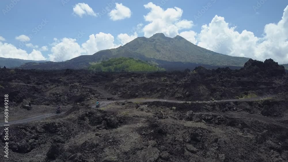 AERIAL CLOSE UP: Young man and woman riding scooters through picturesque stony black lava countryside towards majestic Mount Batur, Bali, Indonesia. Tourists on road trip to Kintamani volcanic crater AERIAL CLOSE UP: Young man and woman riding scooters through picturesque stony black lava countryside towards majestic Mount Batur, Bali, Indonesia. Tourists on road trip to Kintamani volcanic crater
