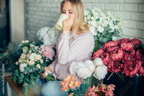 Florist at work. woman in process of making bouquet, holds in her hand a cup of coffee photo