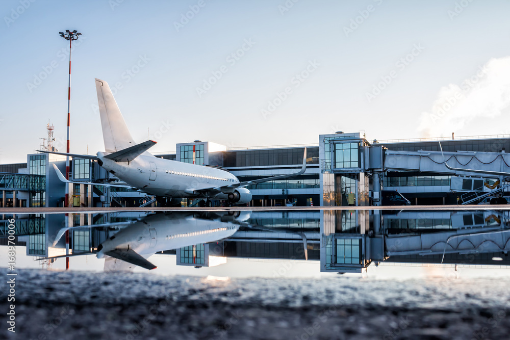 Fototapeta premium Passenger aircraft parked to a jetway with reflection in a puddle