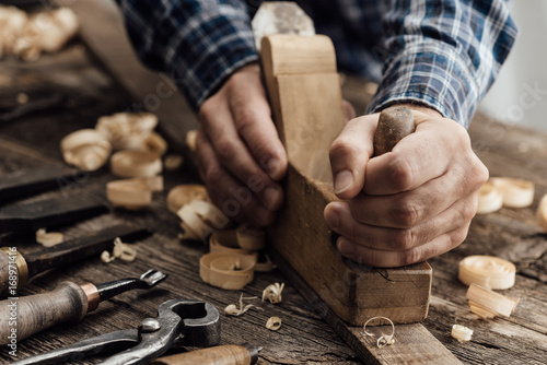 Carpenter working in his workshop, he is smoothing a wooden board using a planer, carpentry, carpentry, woodworking and craftsmanship concept photo