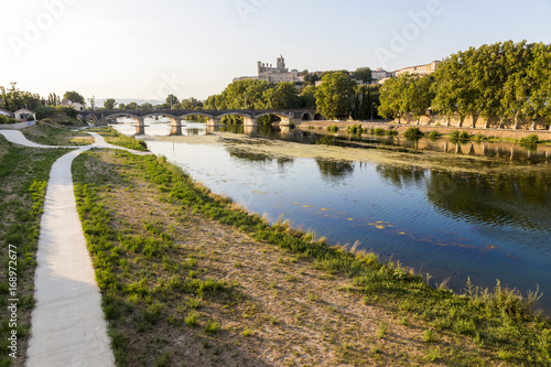 Views at sunset of the French city of Beziers, with trees and one of its bridges reflected over the river Orb, and the 13th-century Cathedral of Saint Nazaire in the background © J. Ossorio Castillo