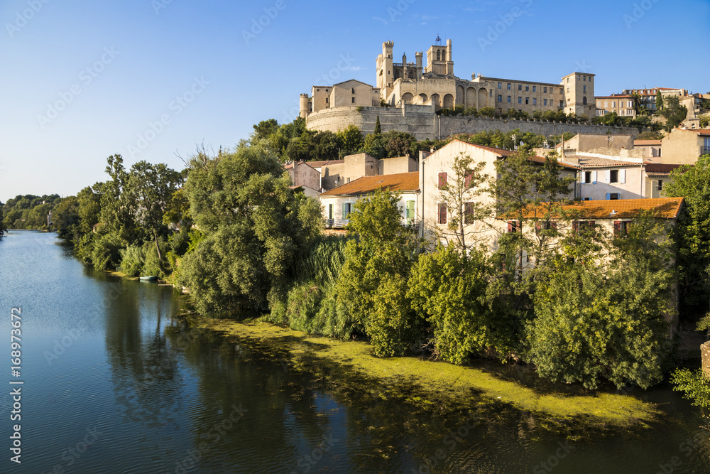 Views at sunset of the French city of Beziers, with trees, the river Orb, and the 13th-century Cathedral of Saint Nazaire in the background