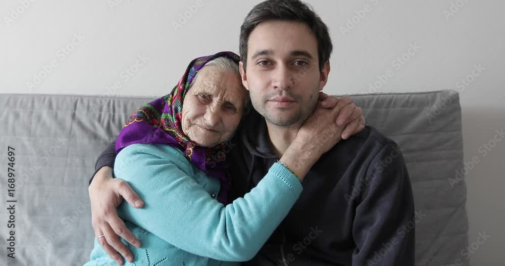 The old grandmother and young grandson are sitting on the couch and hugging. The old grandmother and young grandson are sitting on the couch and hugging.