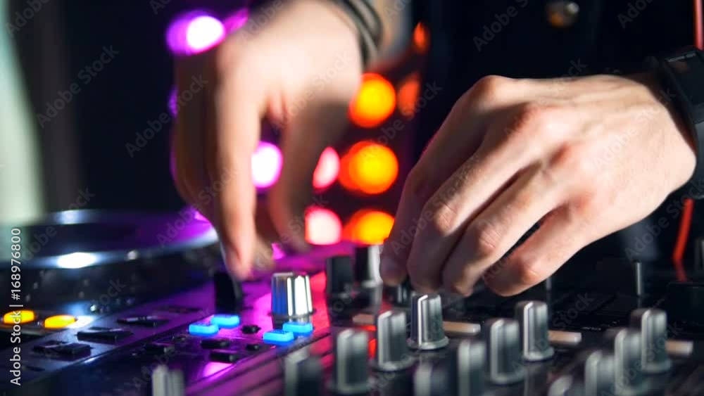 DJs hands twist a turntable and add volume. DJs hands twist a turntable and add volume.