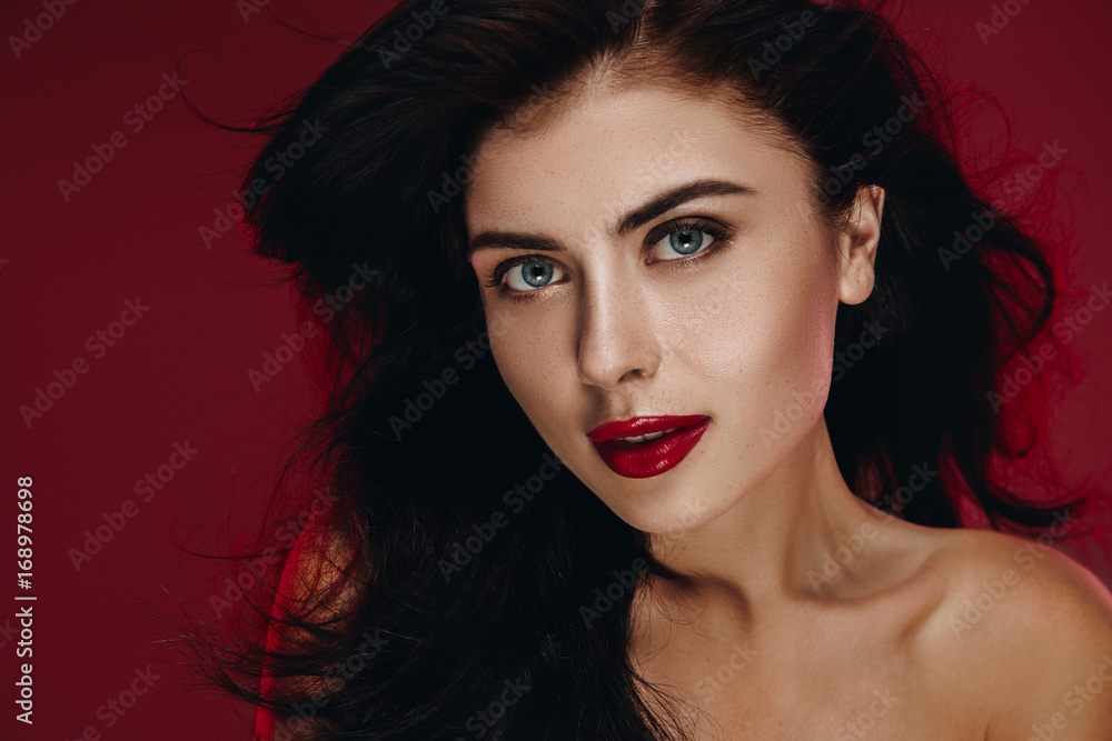 Fototapeta premium Beauty Brunette Woman with Perfect Makeup. Beautiful Professional Holiday Make up. Beauty Girl Face studio portrait isolated on red background