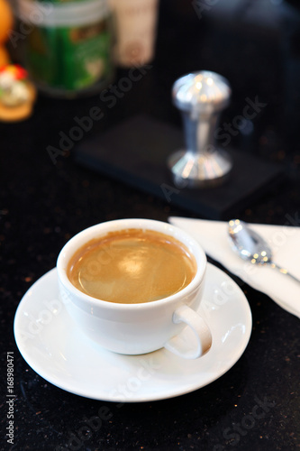 Creammy coffe in white cup on dish with dark background