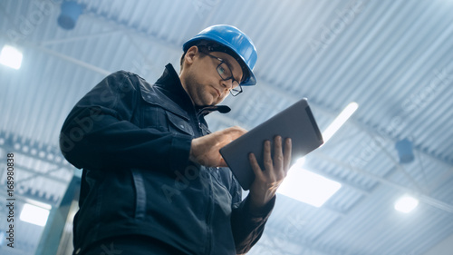 Obraz na płótnie Factory worker in a hard hat is using a tablet computer.
