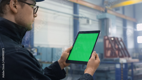 Footage of a tablet with green mock-up screen being used by a worker in industrial environment in a factory.