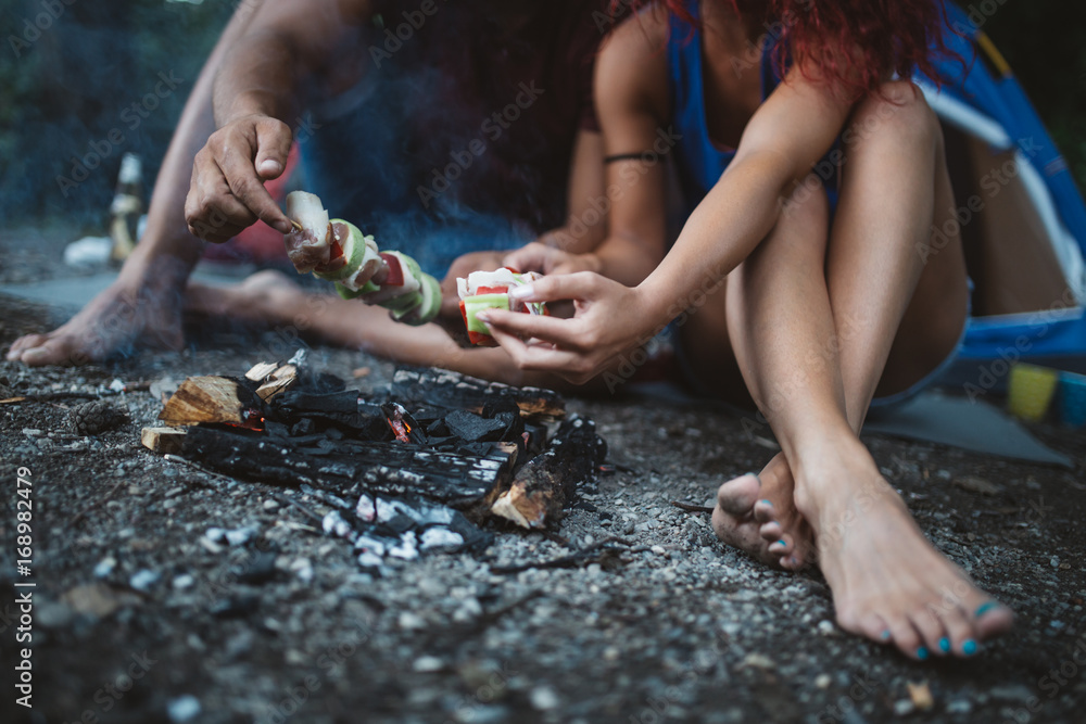 Happy young couple camping and hiking on wild mountain river. They sitting around campfire and making barbecue. Happy young couple camping and hiking on wild mountain river. They sitting around campfire and making barbecue.
