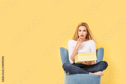 Young woman sits on chair with giftbox in hand and wonder what is inside