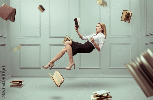 A relaxed woman levitates in a room full of flying books photo
