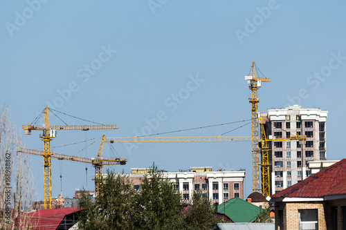 Tower cranes on the construction of new high-rise buildings against the backdrop of old houses.
