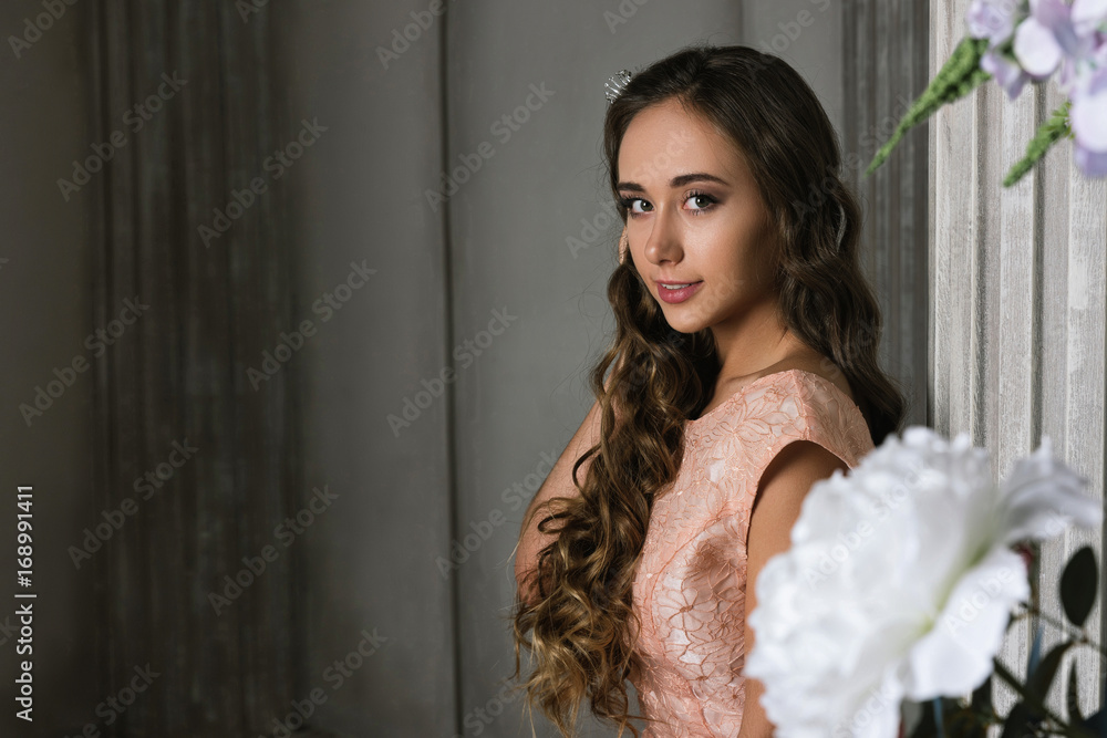 Fototapeta premium Portrait of Beautiful romantic lady with flowers. Beautiful young lady in a pink lacy dress, in a vintage luxury grey interior. long curly hair, fashion makeup