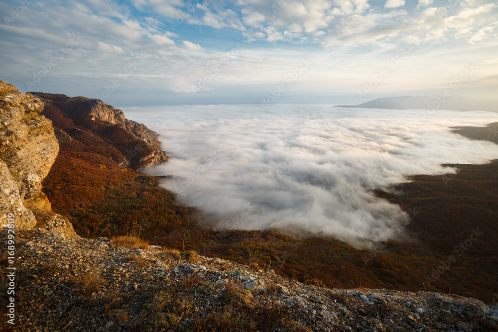Dramatic sunset landscape in yellow autumn high mountains over clouds. Beautiful scenery of sky
