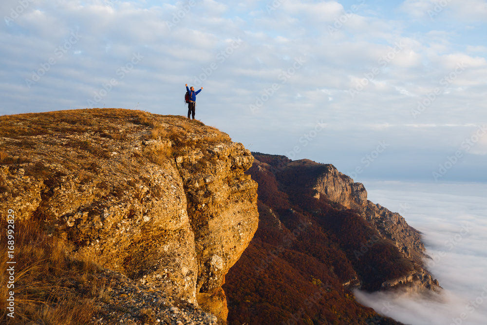 Hiker man cheering with arms spread and raised to the sky after hiking mountain top summit. Climber with backpack on the peak above the clouds. Winner, success, freedom concept.