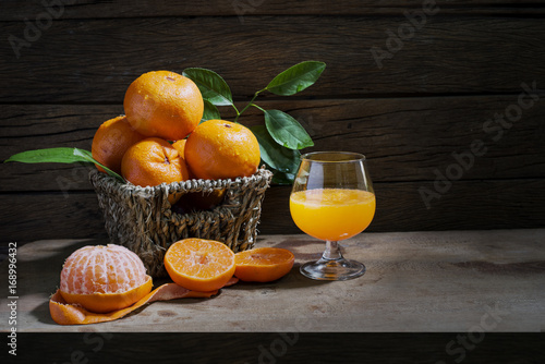 Still life with oranges and basket and glass of juice on a wooden table