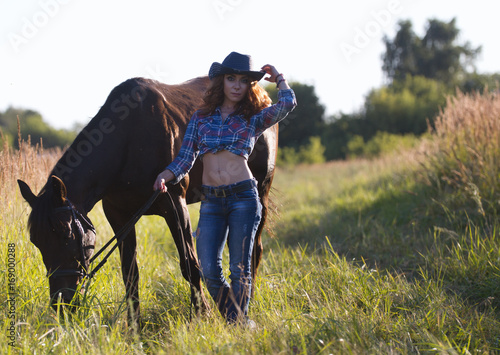 Portrait of a cowgirl - young woman with horse in meadow at summer day