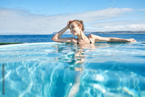 Young cheerful girl swimming in water of pool looking away on background of sea  Iceland  West Fjords. back view