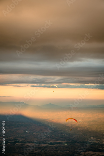 Paragliding from the mountains to the beautiful sunset,Paragliding over mountains, paragliding silhouette flying © Adisak