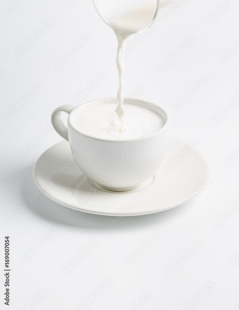 fresh milk is poured from a glass into a cup isolated on white background fresh milk is poured from a glass into a cup isolated on white background