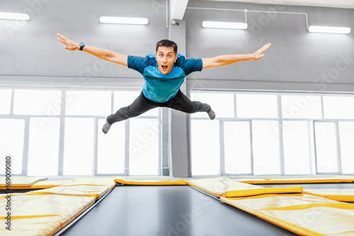 A young fit happy man jumping and flying on trampoline in fitness gym