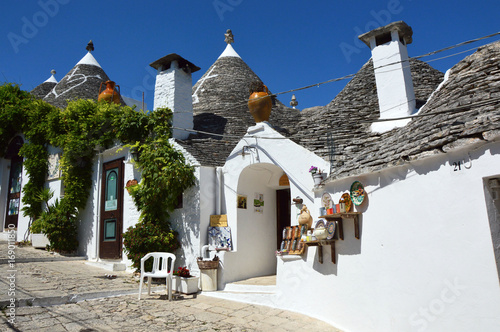 Beautiful street of Alberobello with trulli houses among green plants and flowers, main touristic district, Apulia region, Southern Italy photo