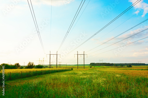 High voltage steel electricity transmission lines pylons of a power line on a green field. Scenery rural summer landscape. Supply, distribution, transmitting energy concept.