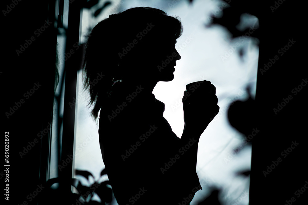 woman silhouette with a cup of hot drink in a window
