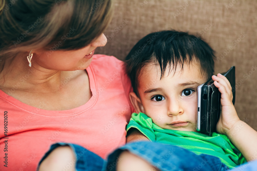 Portrait of a family at home, mom holding on hands a child with smartphone