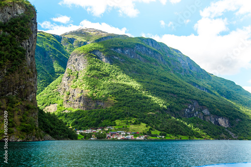Small village with a lovely backdrop at Flam Fjords, Norway. Mountains and fjord in Norway. Clouds and blue sky. Beautiful stunning views of mountains, water, sky, clouds and sun. Norwegian nature.
