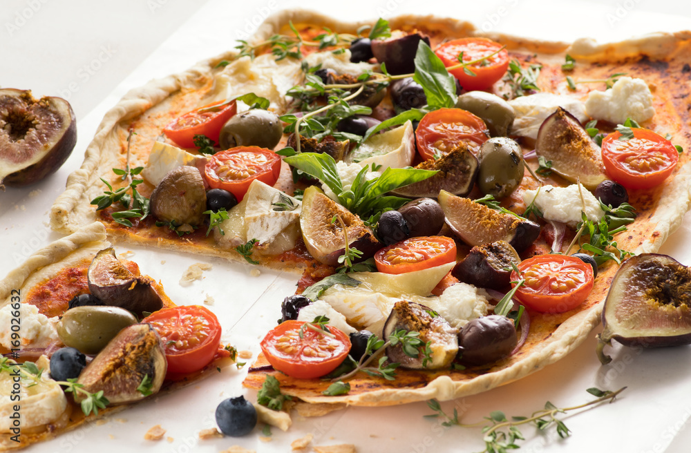 Homemade flatbread pizza with tomato,basil,fig,blueberries,cheese,olives and herbs. Close up.