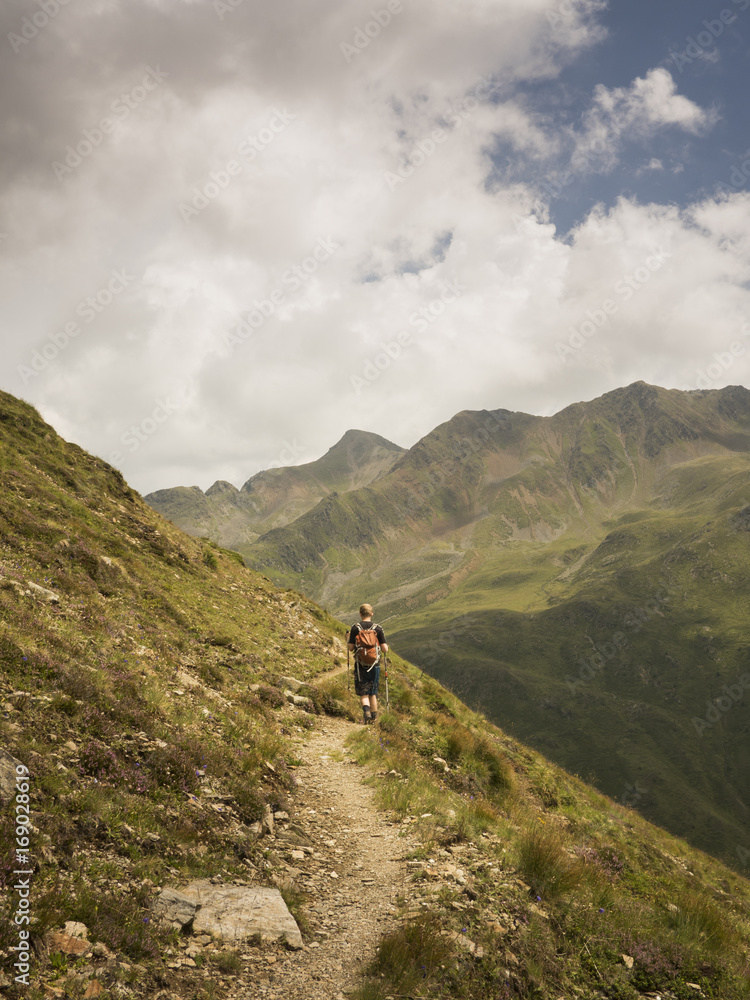 Hiker along a trail in the alps with view over a green valley